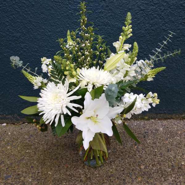 White floral arrangement in a glass vase with lilies and chrysanthemums