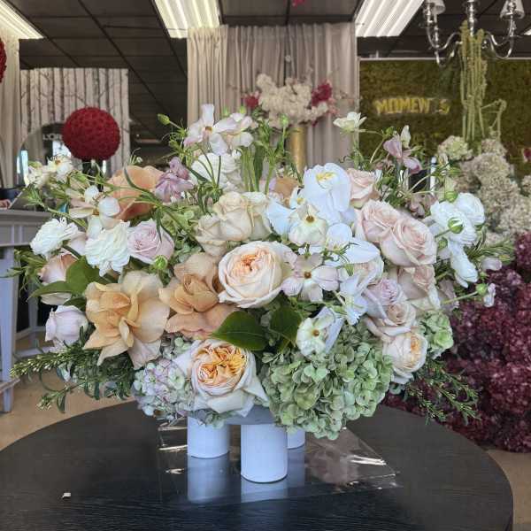 Large pastel floral arrangement with roses and orchids in white cylinders