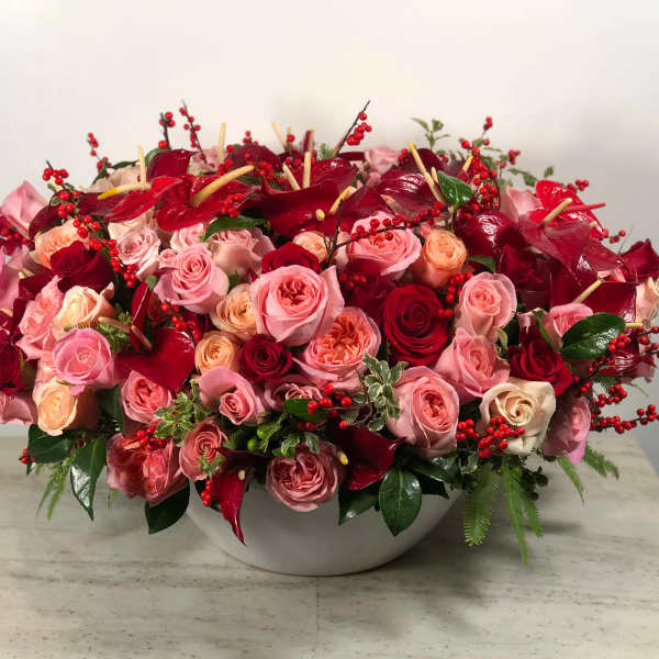 Large pink and red rose arrangement in a white bowl vase