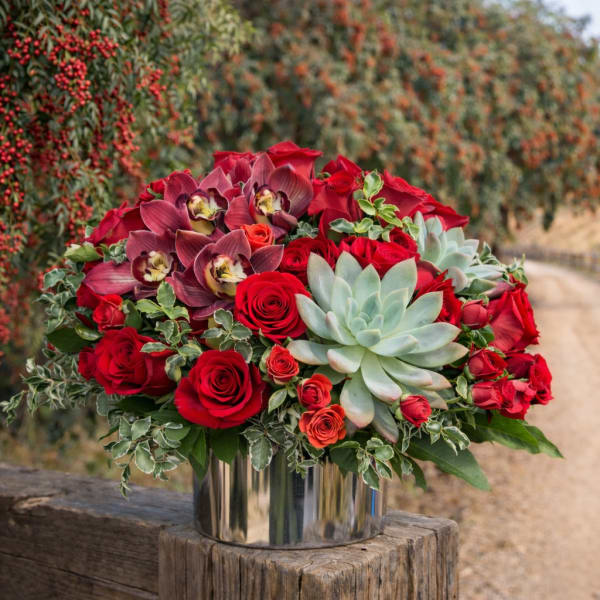 Red roses and orchids arranged with succulents in a silver vase