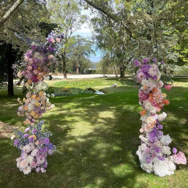 Two tall floral columns in pastel purple, pink, and white outdoors
