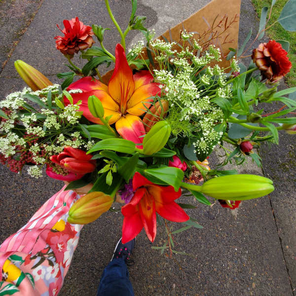 Handheld bouquet of red and orange lilies with small white filler flowers in kraft paper wrap