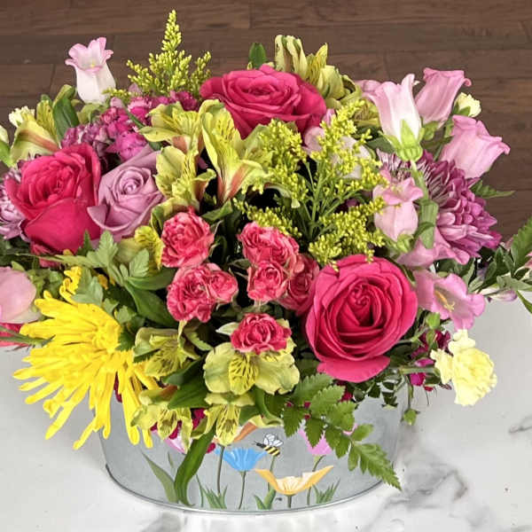 Mixed bouquet in a round tin container with pink and yellow flowers