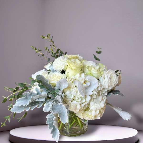 White floral bouquet in a clear glass vase with silvery foliage