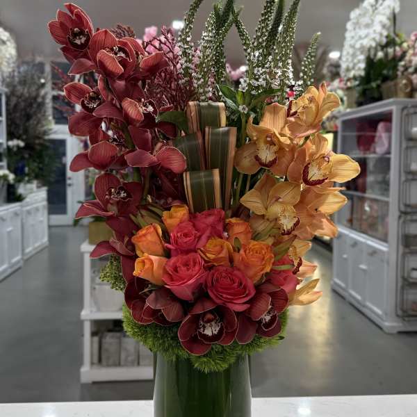 Tall arrangement of orchids and roses in a green glass vase