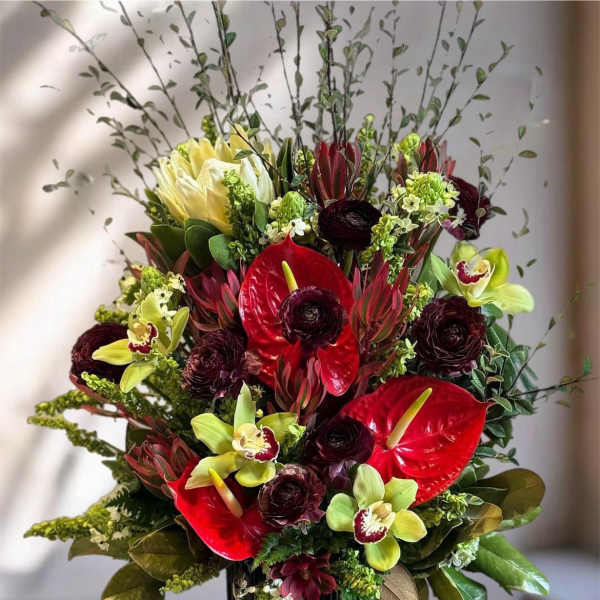 Red anthuriums and green orchids in a black vase