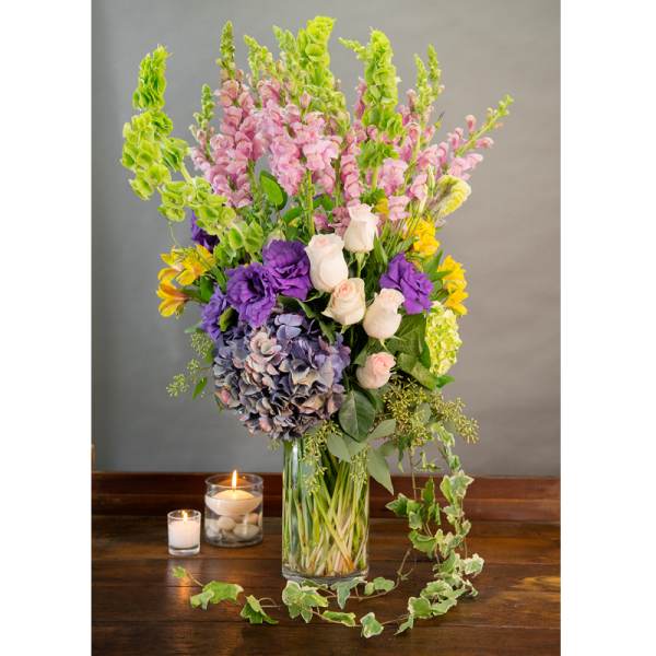 Tall mixed bouquet in a glass vase with candles beside it