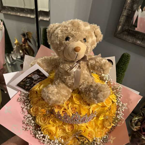 Teddy bear sitting on a yellow rose bouquet with pink wrapping