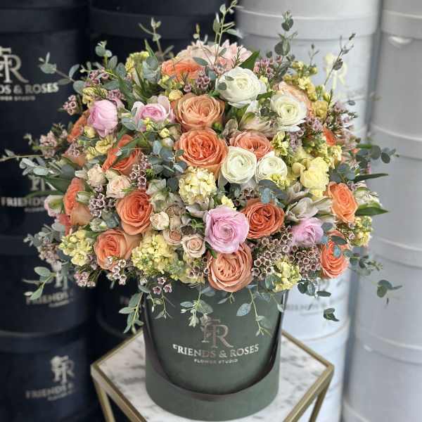 Mixed pastel roses and small filler flowers in a dark green hatbox