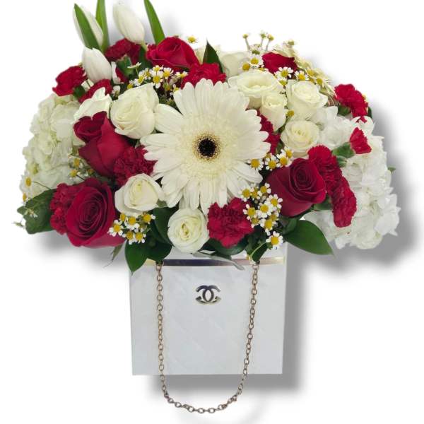 Red and white mixed flower arrangement with gerbera, roses, and tulips in a white box with chain handle