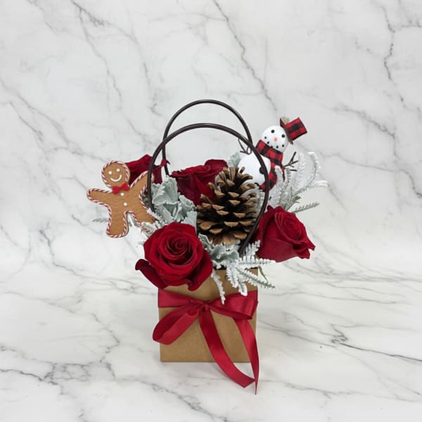 Red roses in a gift bag with a pinecone and holiday decorations