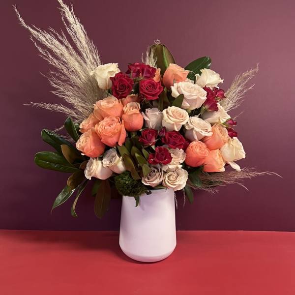 Mixed roses in a white vase with tall dried grass accents