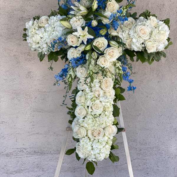 White floral cross arrangement with blue accents on an easel