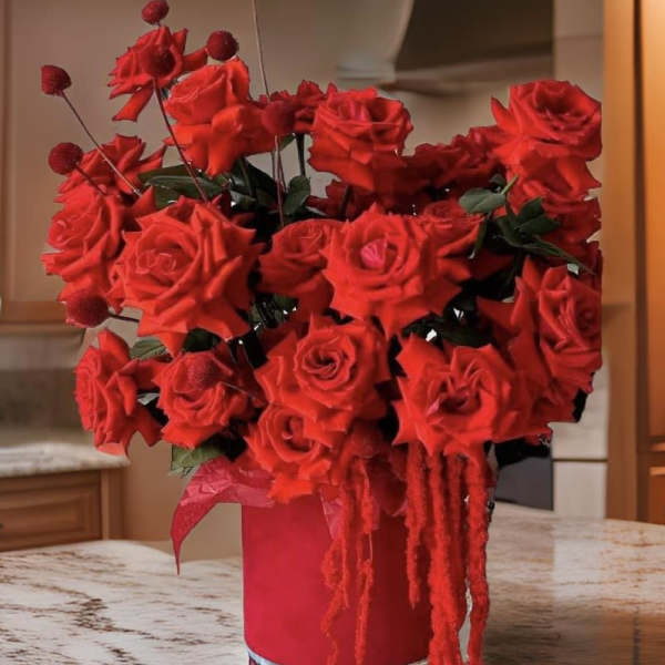 Red rose arrangement in a tall red vase with hanging red accents