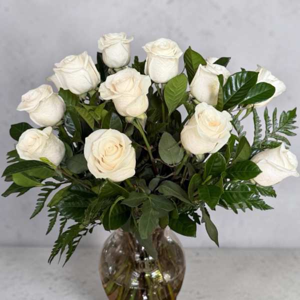 White roses arranged in a glass vase with dark green foliage