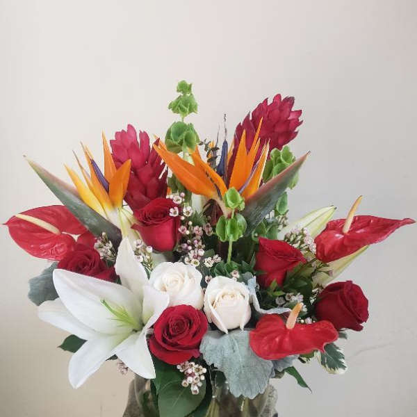 Tropical bouquet with red roses, white lilies, and bird-of-paradise in a glass vase