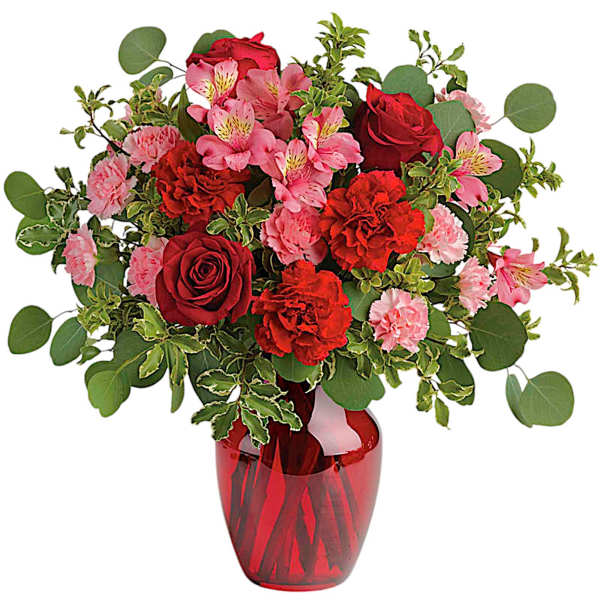 Red roses and pink flowers arranged in a red glass vase