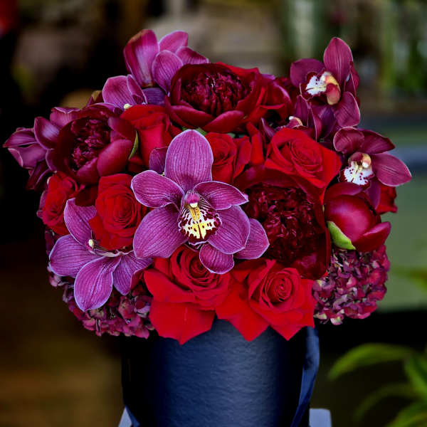 Red roses and purple orchids arranged in a black hatbox
