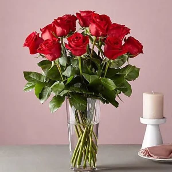 Red roses arranged in a clear glass vase beside a white candle