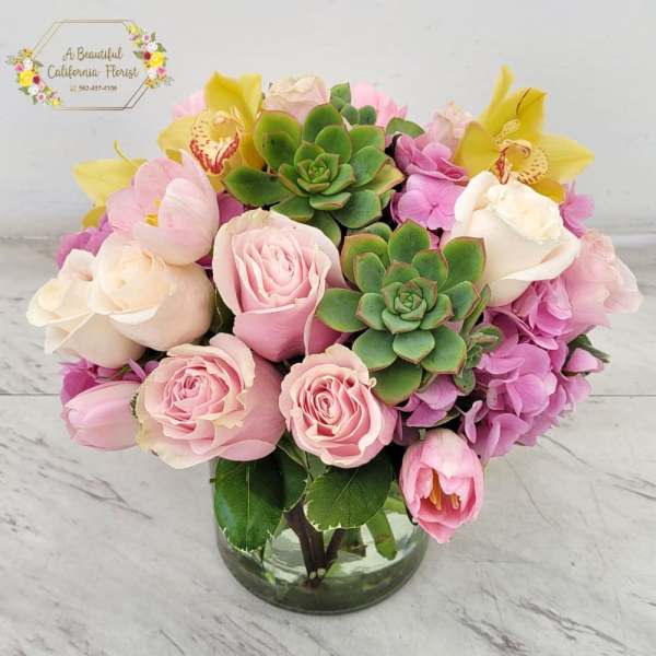 Pink roses, yellow orchids, and green succulents in a glass vase