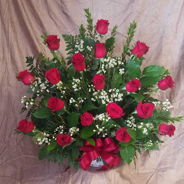 Red roses arranged in a basket with baby's breath and a red ribbon