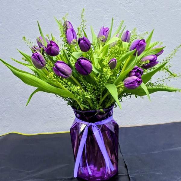 Purple tulips arranged in a purple vase with a ribbon