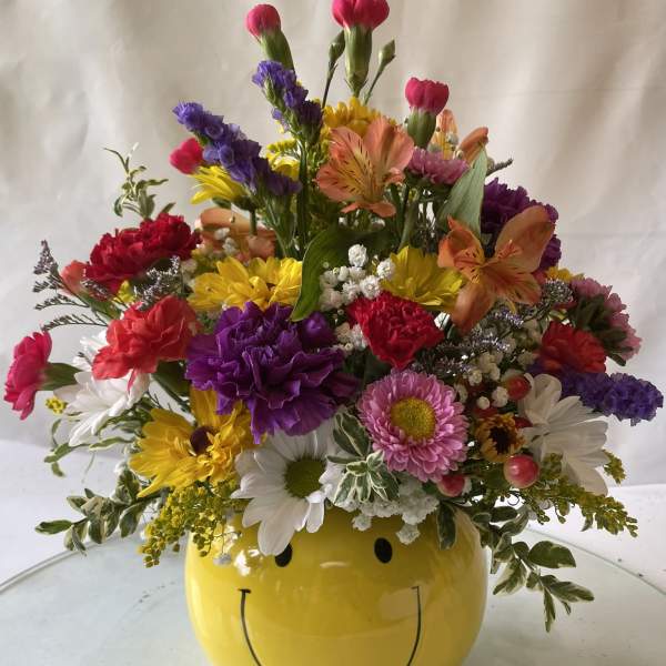 Colorful mixed flower arrangement in a yellow smiley-face vase