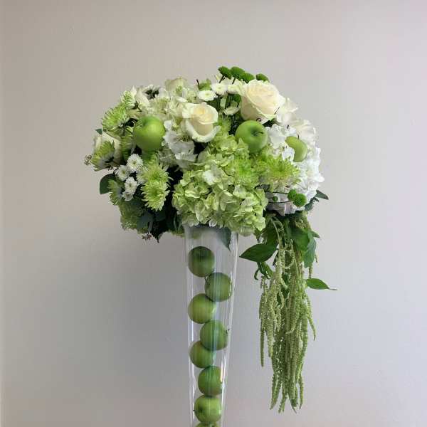 White and green floral arrangement in a tall clear vase with apples inside