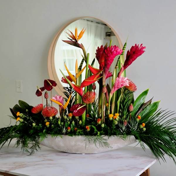 Tropical flower arrangement in a low white bowl with pink and orange blooms