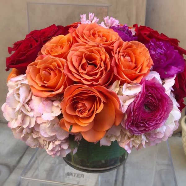 Round bouquet of orange, red, pink, and purple flowers in a glass vase