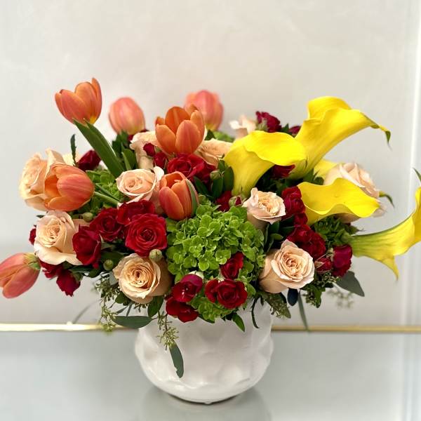 Bouquet of red and peach roses with orange tulips and yellow calla lilies in a white vase