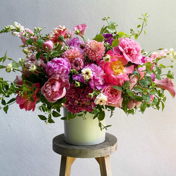 Large pink and peach flower arrangement in a pale vase