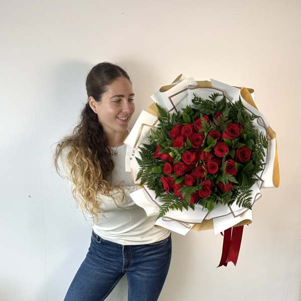 Woman holding a large bouquet of red roses wrapped in white paper
