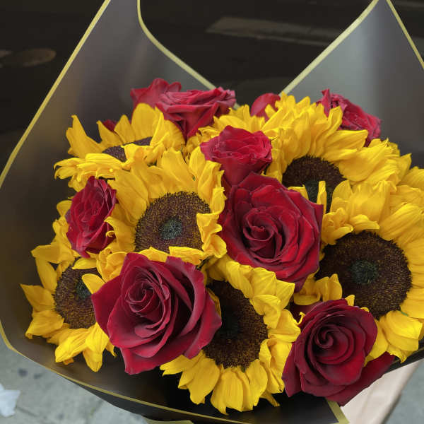 Bouquet of yellow sunflowers and red roses wrapped in black paper with gold trim.
