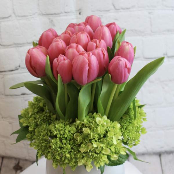 Pink tulips arranged in a white vase with green hydrangeas