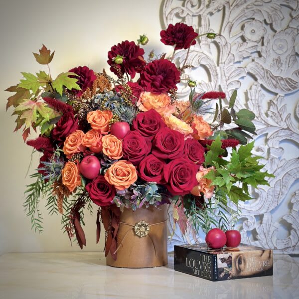 Bouquet of red and peach roses in a gold vase with decorative foliage