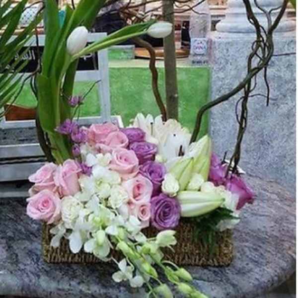 Basket arrangement of pink and purple roses with white lilies and arching branches