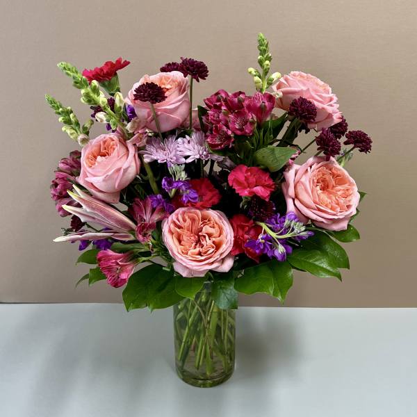 Pink roses and mixed flowers arranged in a clear glass vase