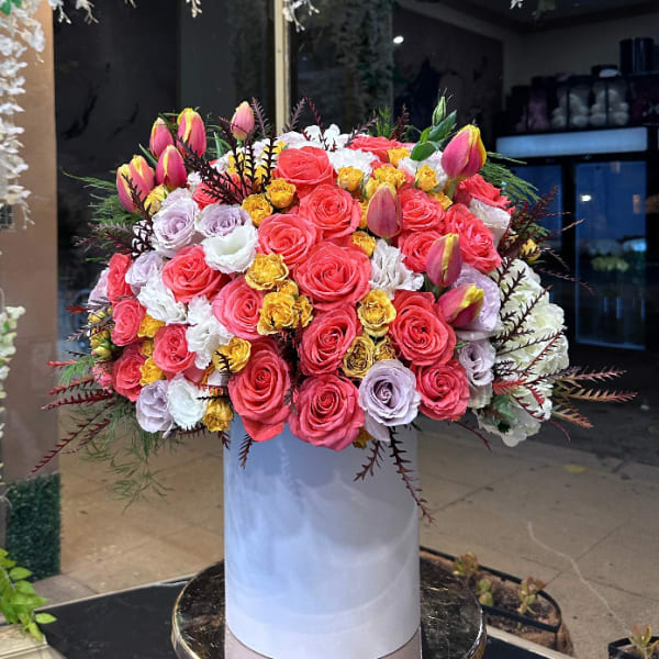 Large bouquet of pink, white, and yellow roses in a tall white box
