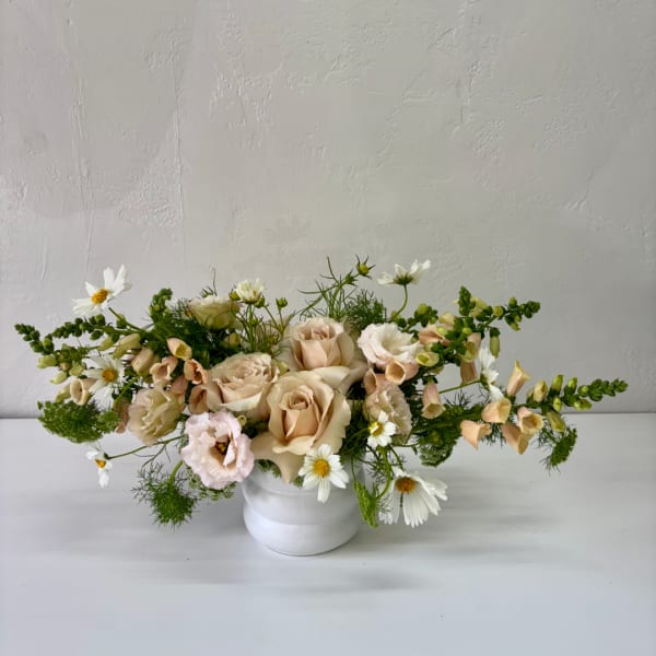 Low floral arrangement of blush roses and white daisies in a white vase