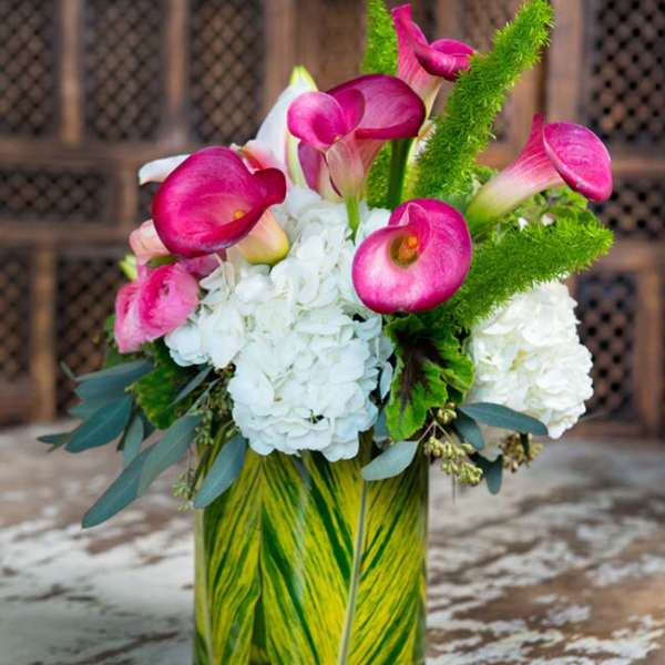 Pink calla lilies with white hydrangeas in a glass vase