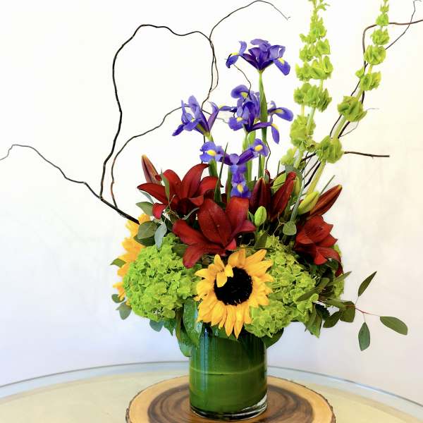 Colorful floral arrangement with sunflowers, red lilies, and purple irises in a green vase