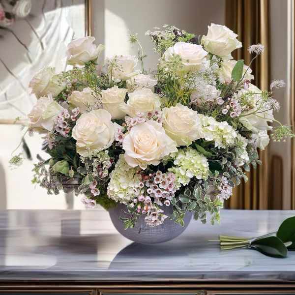 Cream rose arrangement in a gray vase with small pink filler flowers