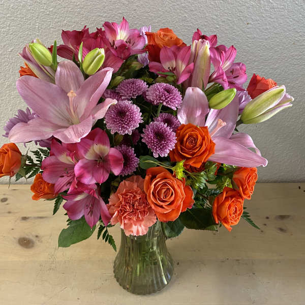 Bouquet of pink lilies, orange roses, and purple mums in a glass vase