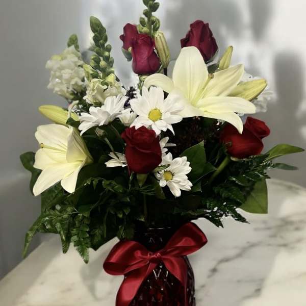 Red roses and white lilies in a red glass vase with a satin bow