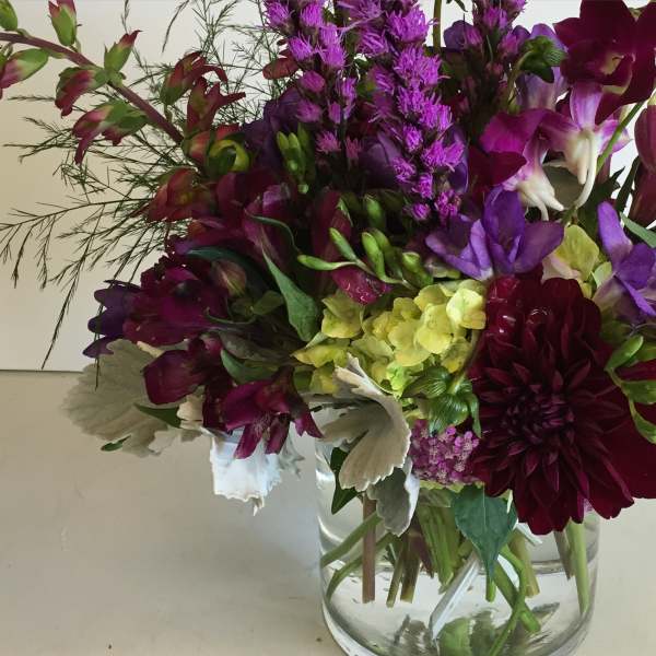 Mixed bouquet of purple and burgundy flowers in a clear glass vase