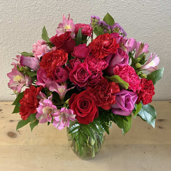 Bouquet of red and pink roses, carnations, and alstroemeria in a glass vase