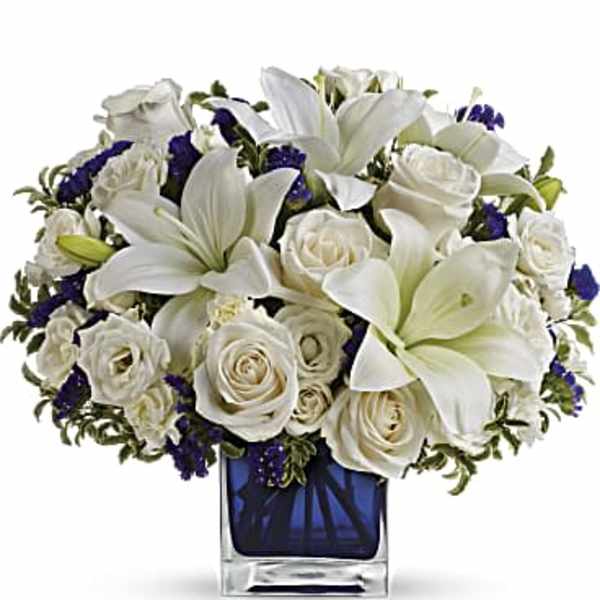 White lilies and roses arranged in a blue glass vase