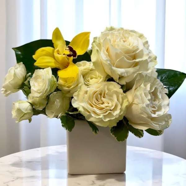 Cream roses and a yellow orchid in a white vase