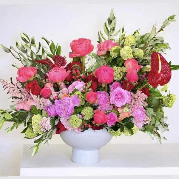 Bright pink and red floral arrangement in a white pedestal vase